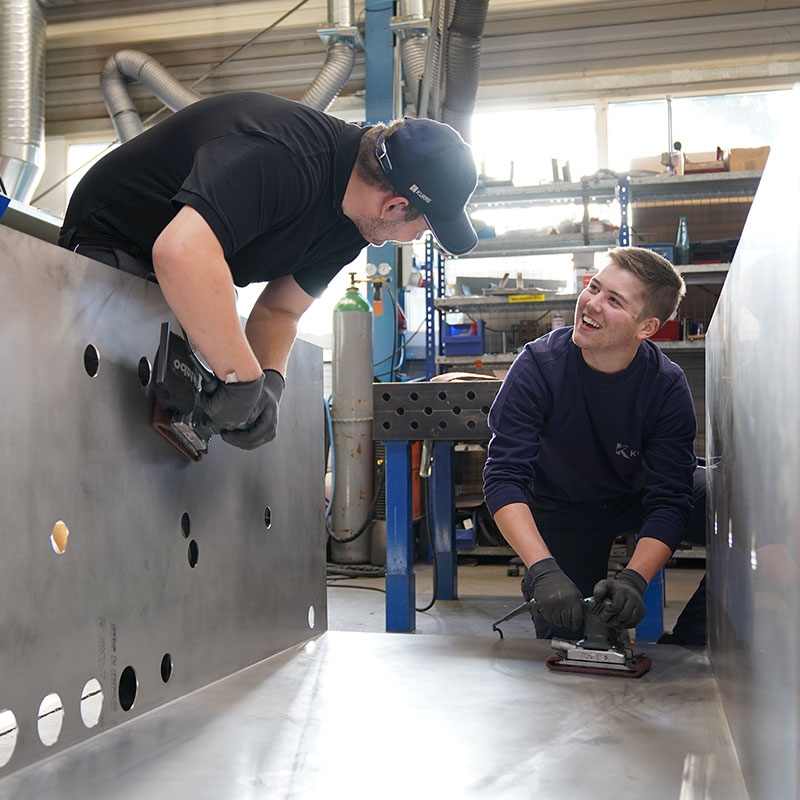Two trainees are grinding an assembly and smiling at each other