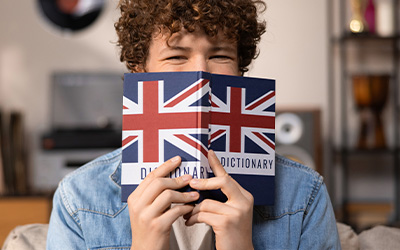 Lachende Person hält sich ein englisches Wörterbuch vor das Gesicht
