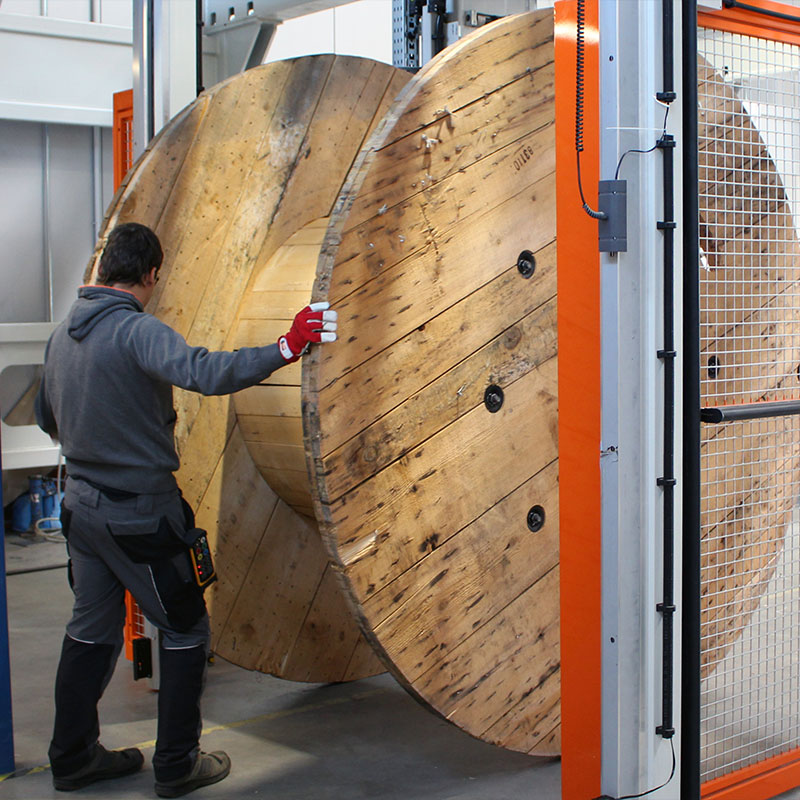 Mitarbeiter rollt eine große Holzspule in einen Portalwickler der Firma KURRE
