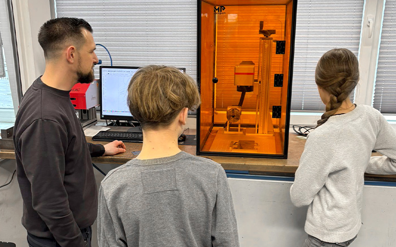 Ein Kurre-Mitarbeiter und zwei Kinder blicken auf ein Lasergerät.